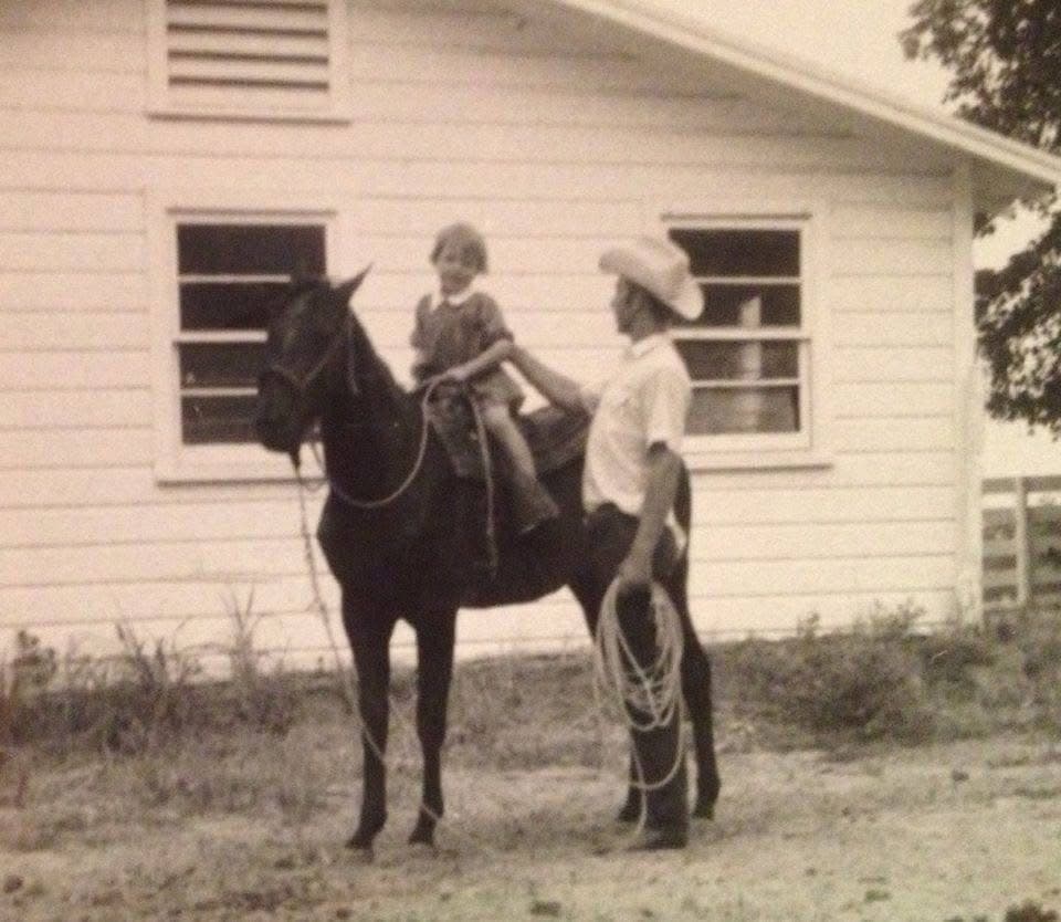 Rufus leading a young Jill on horseback outside the family home